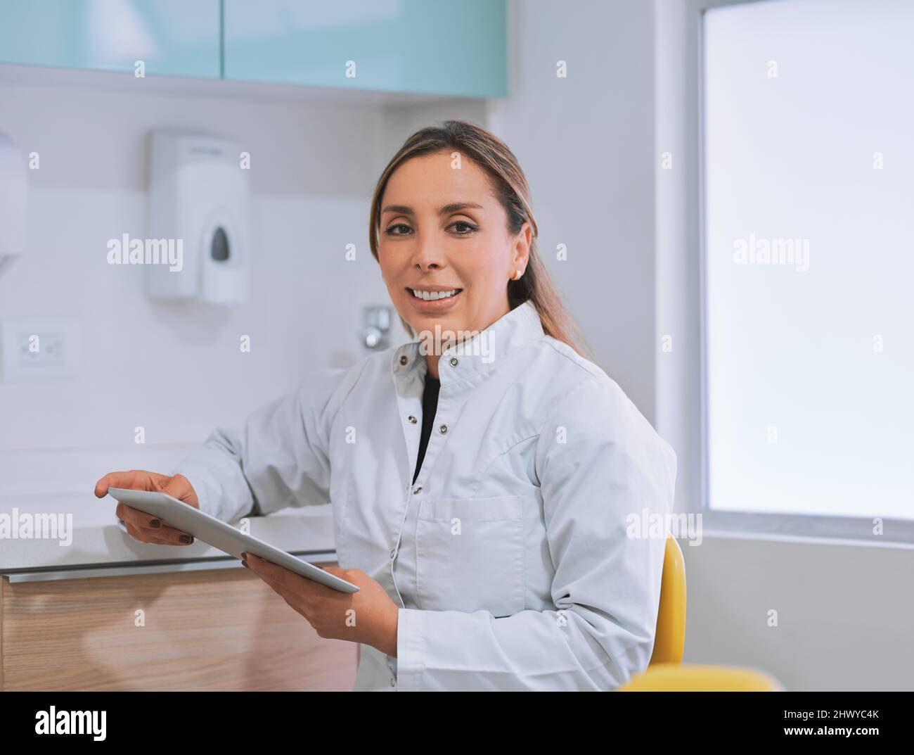 Looking after your oral health. Portrait of a cheerful young female dentist working on her digital tablet while looking at the camera in her office. Stock Photo
