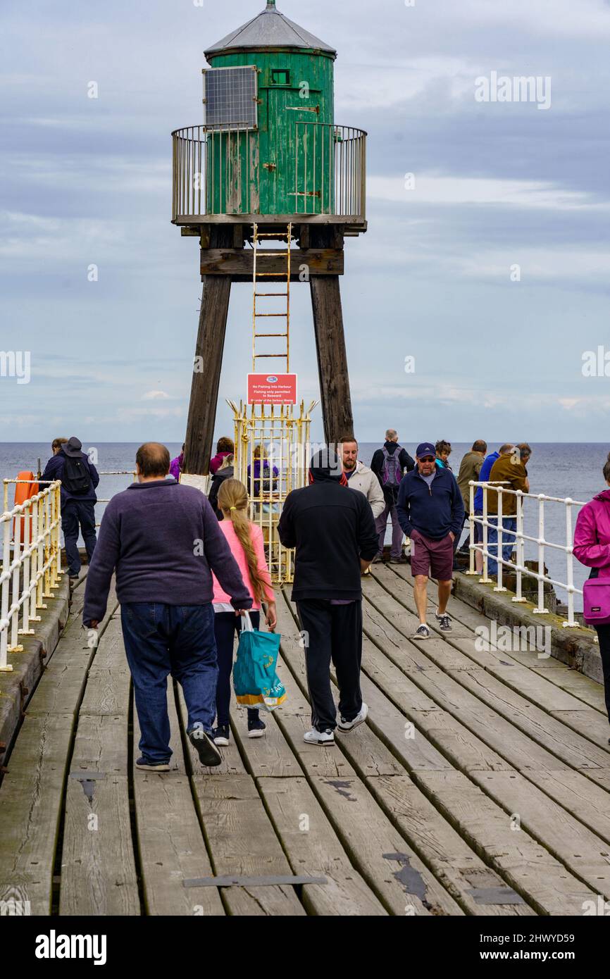 Whitby East Pier in North Yorkshire features a little green wooden lighthouse where tourists may rest and enjoy the view of the shore. Stock Photo