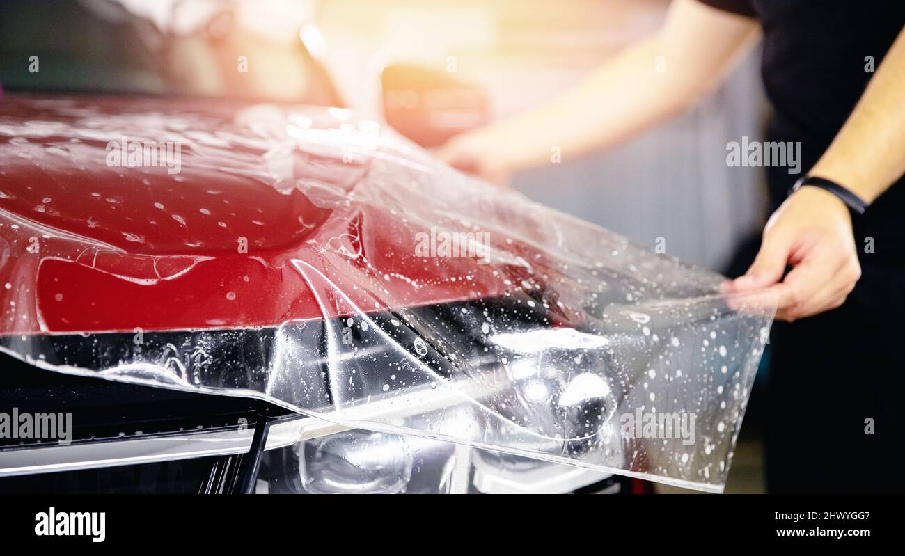 Process of pasting hood of red car with protective vinyl film from