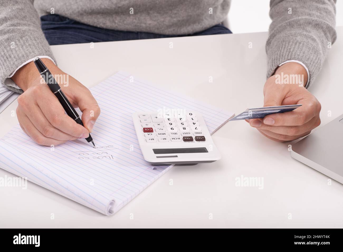 Calculating what I spent this month. A close up of a man holding a credit card writing something on his notepad whilst using a calculator. Stock Photo