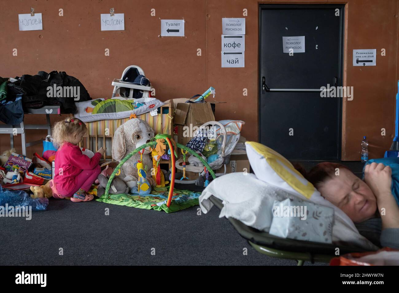 Krakow, Poland. 08th Mar, 2022. A women seen sleeping on the camp-bed close to a girl playing with her toys in the sports hall of the Cracovia club where accommodation was organised for refugees from Ukraine coming to Krakow. Credit: SOPA Images Limited/Alamy Live News Stock Photo