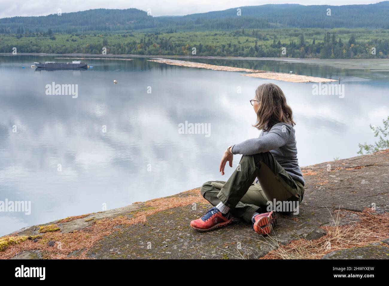 Female tourist sitting on a stone ledge overlooking an inlet at Ripple Rock Hiking Trail, Seymour Narrows, Discovery Passage, British Columbia, Canada Stock Photo