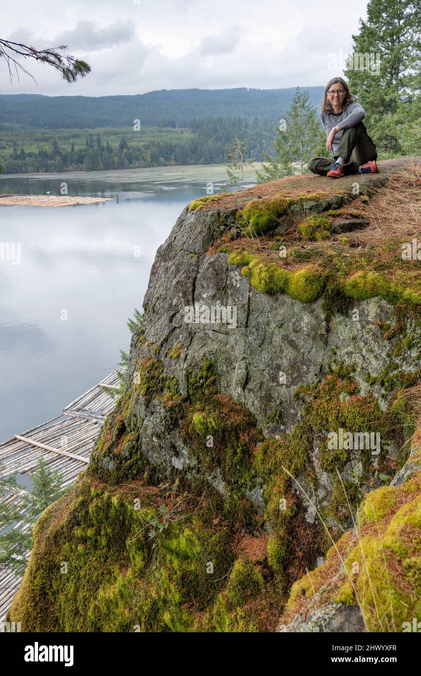Female tourist sitting on a stone ledge overlooking an inlet at Ripple Rock Hiking Trail, Seymour Narrows, Discovery Passage, British Columbia, Canada Stock Photo