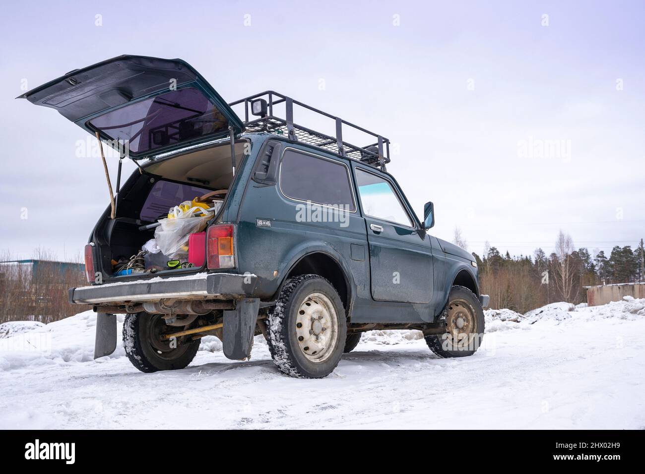 An old brutal classic 4x4 SUV stands with an open trunk on a snowy winter road. Stock Photo