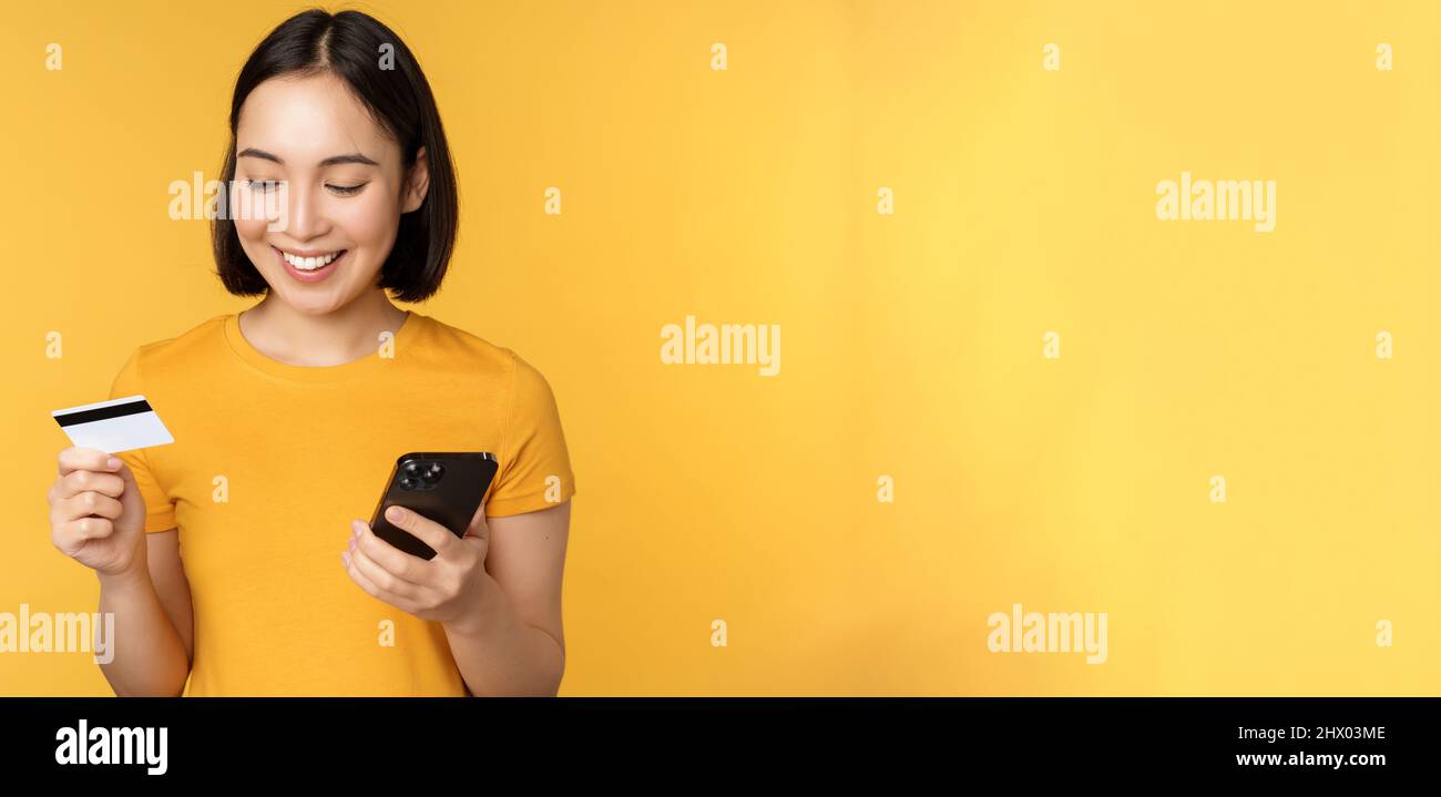 Online shopping. Smiling asian girl using credit card and mobile phone app, paying contactless