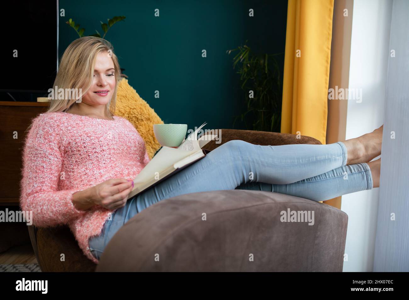 A girl reads a book with a cup in her hand while resting. Stock Photo