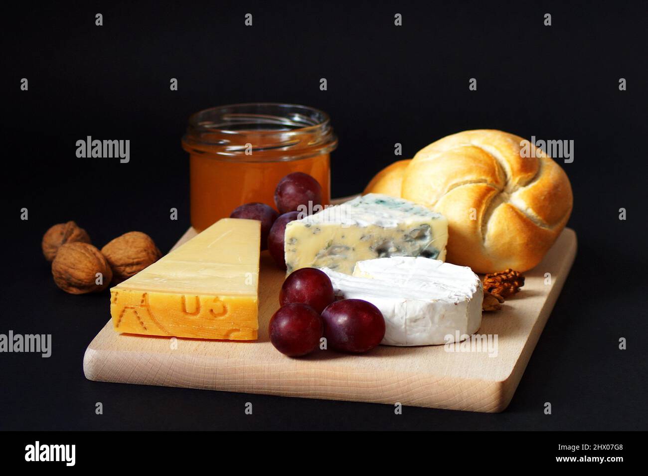 three types of cheese, honey, buns, grapes and nuts on a black background Stock Photo