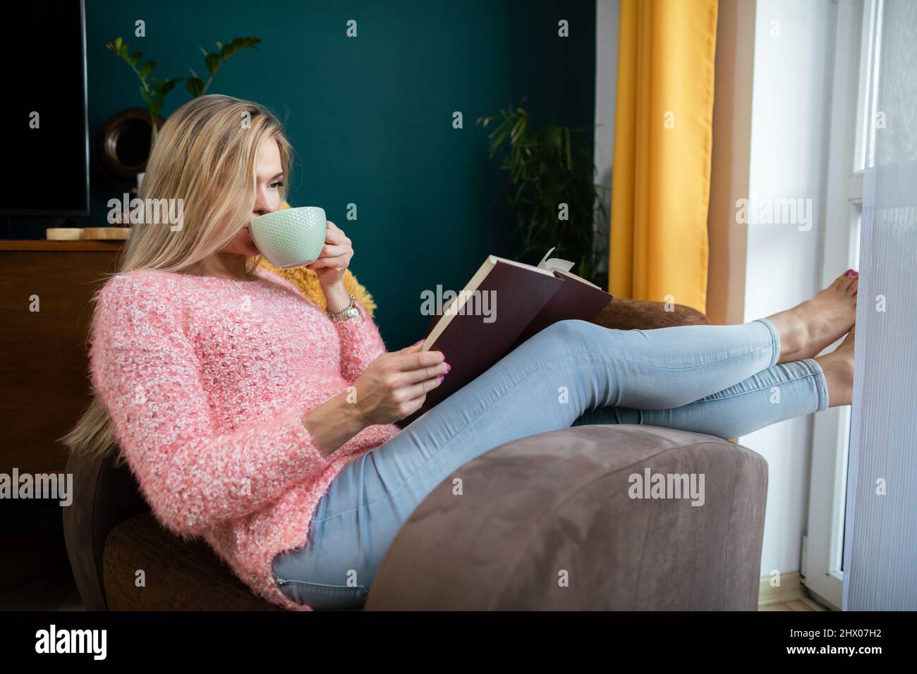 A girl relaxes by reading a book and drinking coffee. Stock Photo