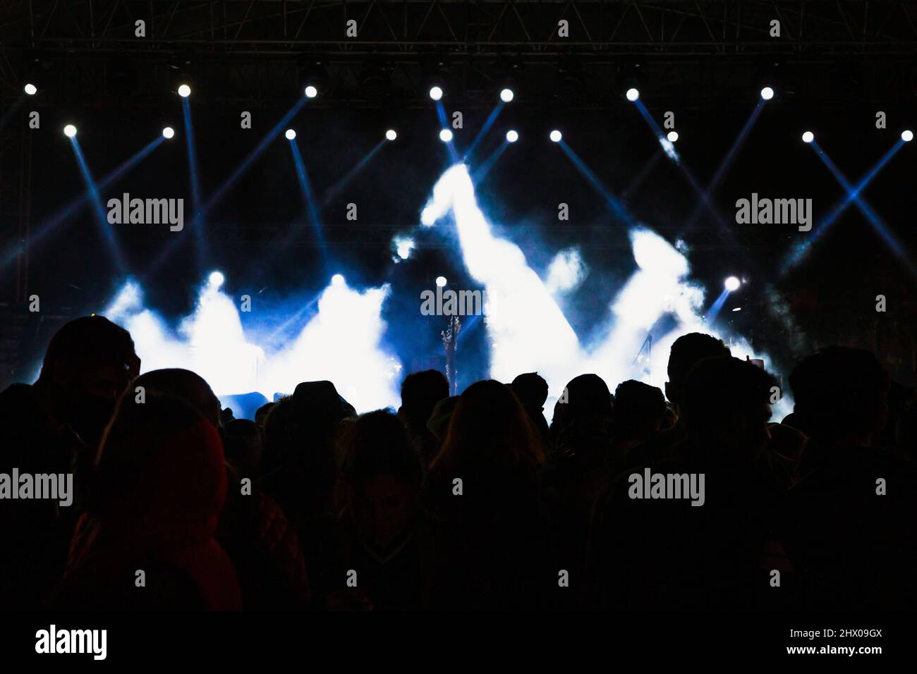 Silhouette of crowd in a concert. Spotlights on the stage. Musical performance background photo. Noise included. Stock Photo