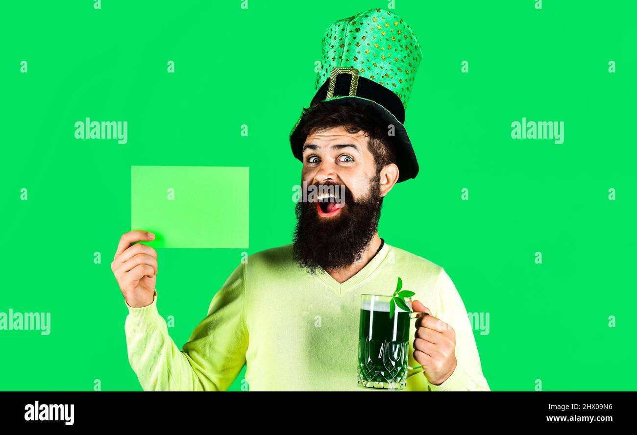 Patricks Day. Happy Bearded man in hat with green beer holds board with copy space for advertising. Stock Photo