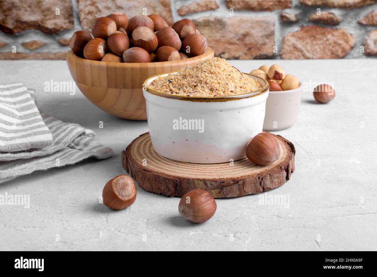 Raw Organic Ground Hazelnut Flour in a Bowl with whole nuts on grey