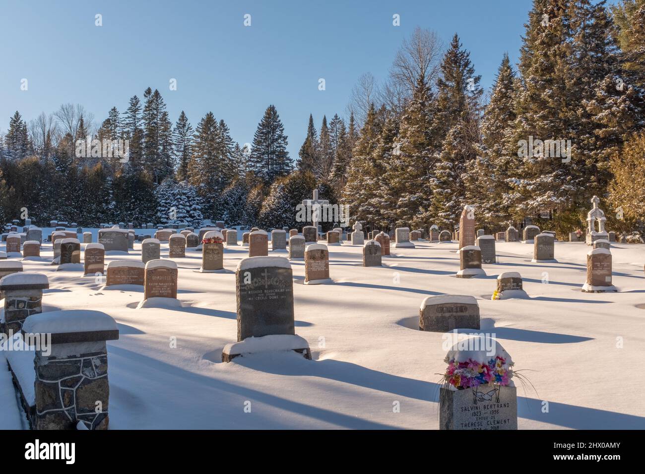 A Canadian cemetery in winter located in Saint-Adolph-d'Howard, Quebec with a cross and headstones covered with snow, taken on a sunny day Stock Photo