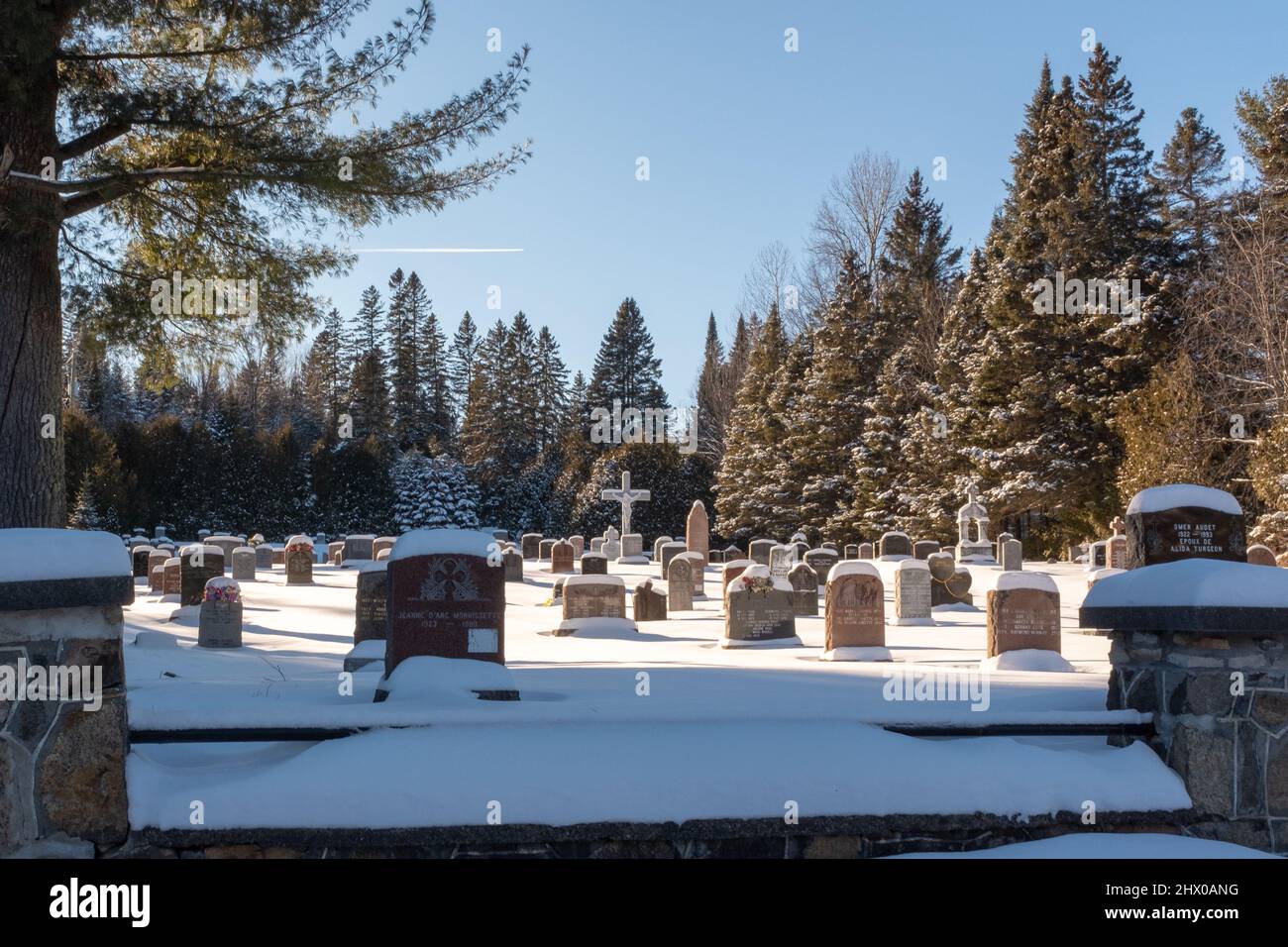 A Canadian cemetery in winter located in Saint-Adolph-d'Howard, Quebec with a cross and headstones covered with snow, taken on a sunny day Stock Photo