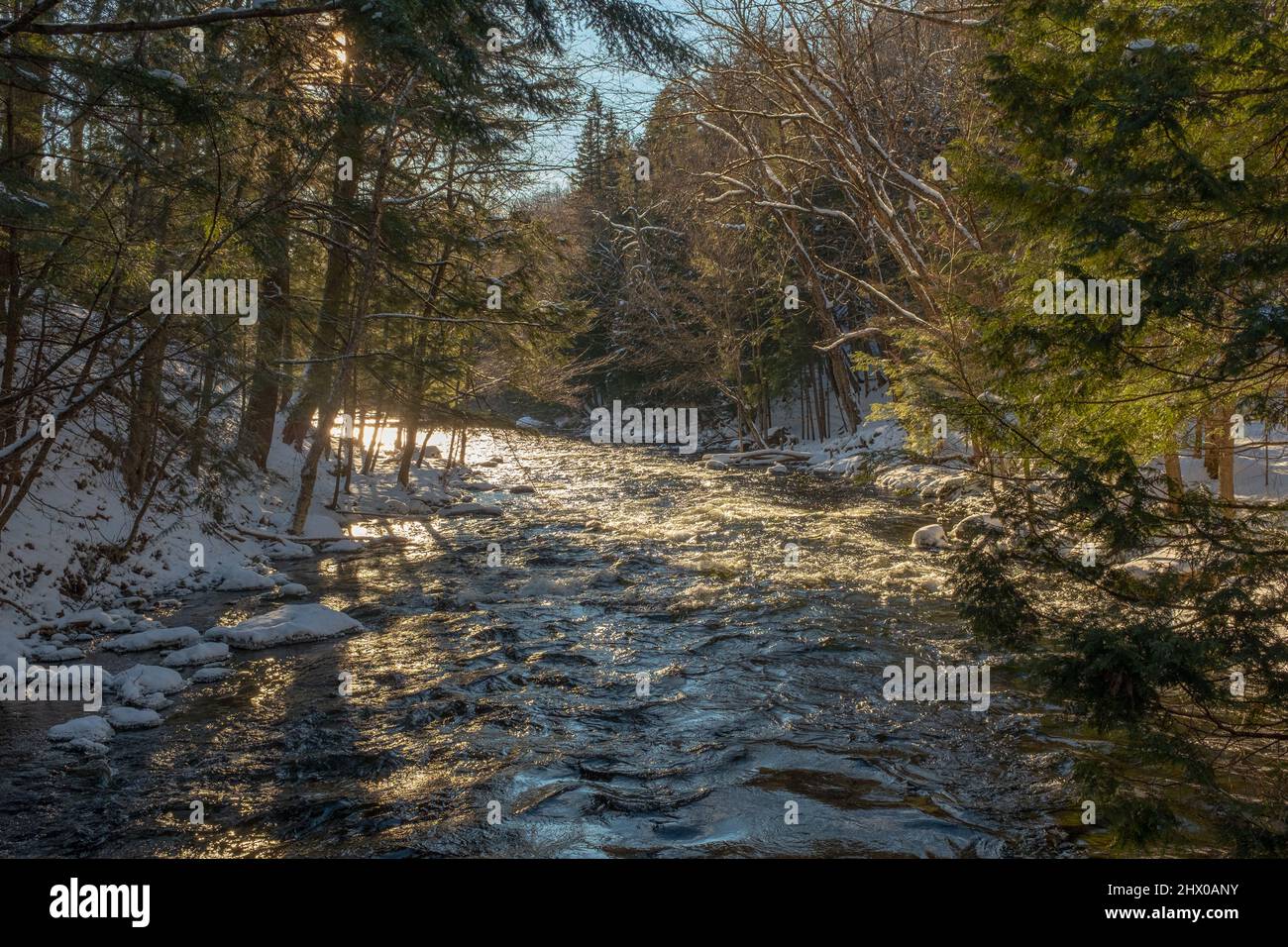 Sun rays reflecting in the rapids of a small river taken in Mont-Tremblant, Quebec, Canada at the end of a sunny winter day with snow on the ground Stock Photo