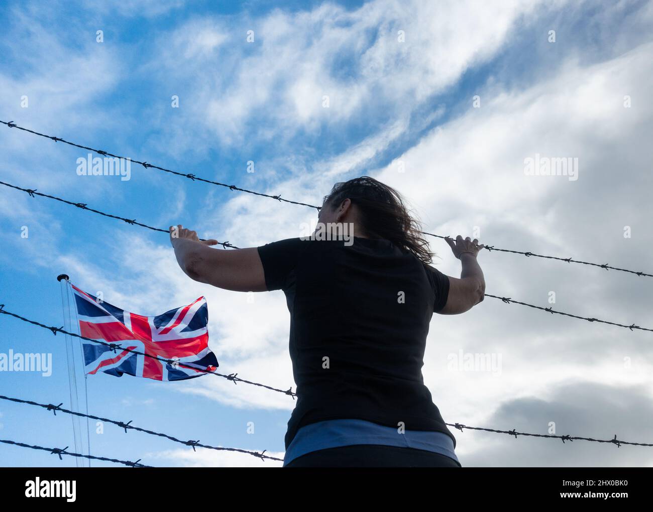 Rear view of woman at border fence control with UK flag. UK immigration, visa policy, Ukraine, Russia conflict refugee, Brexit, EU border... concept Stock Photo