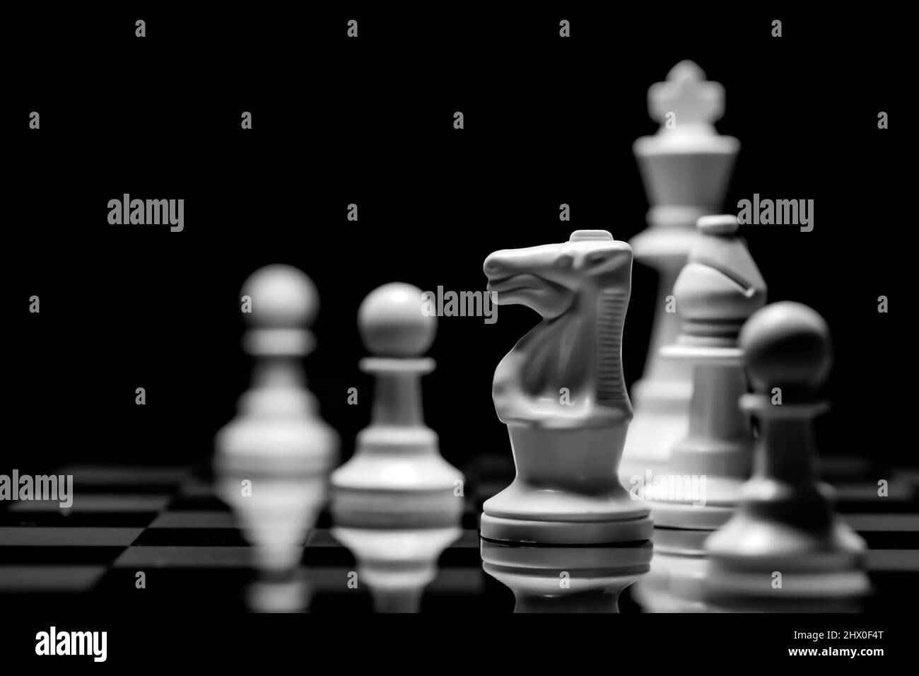 Close up of Chess pieces on a reflective mirror board surface with a plain black background Stock Photo