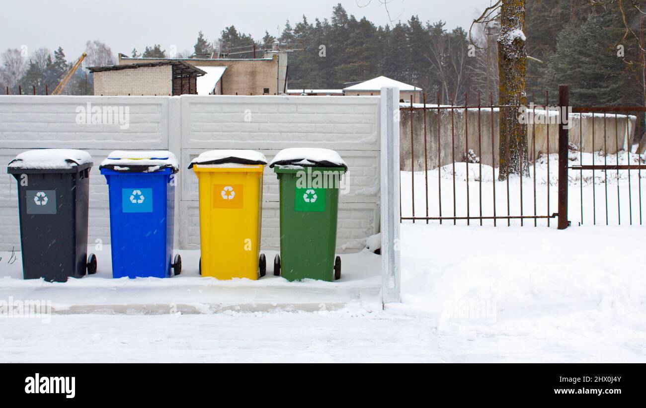 Four plastic trash cans near the fence in winter. The containers are located in the courtyard of the residential area. Separate waste sorting. Respons Stock Photo