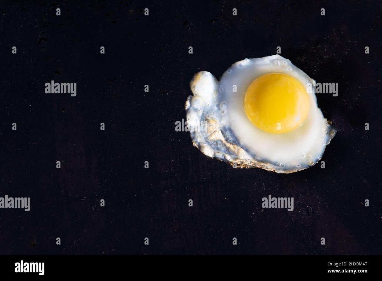 Single fried quail egg. Fried on a flat top griddle. Bright yellow yolk on a greasy black flat top. Stock Photo