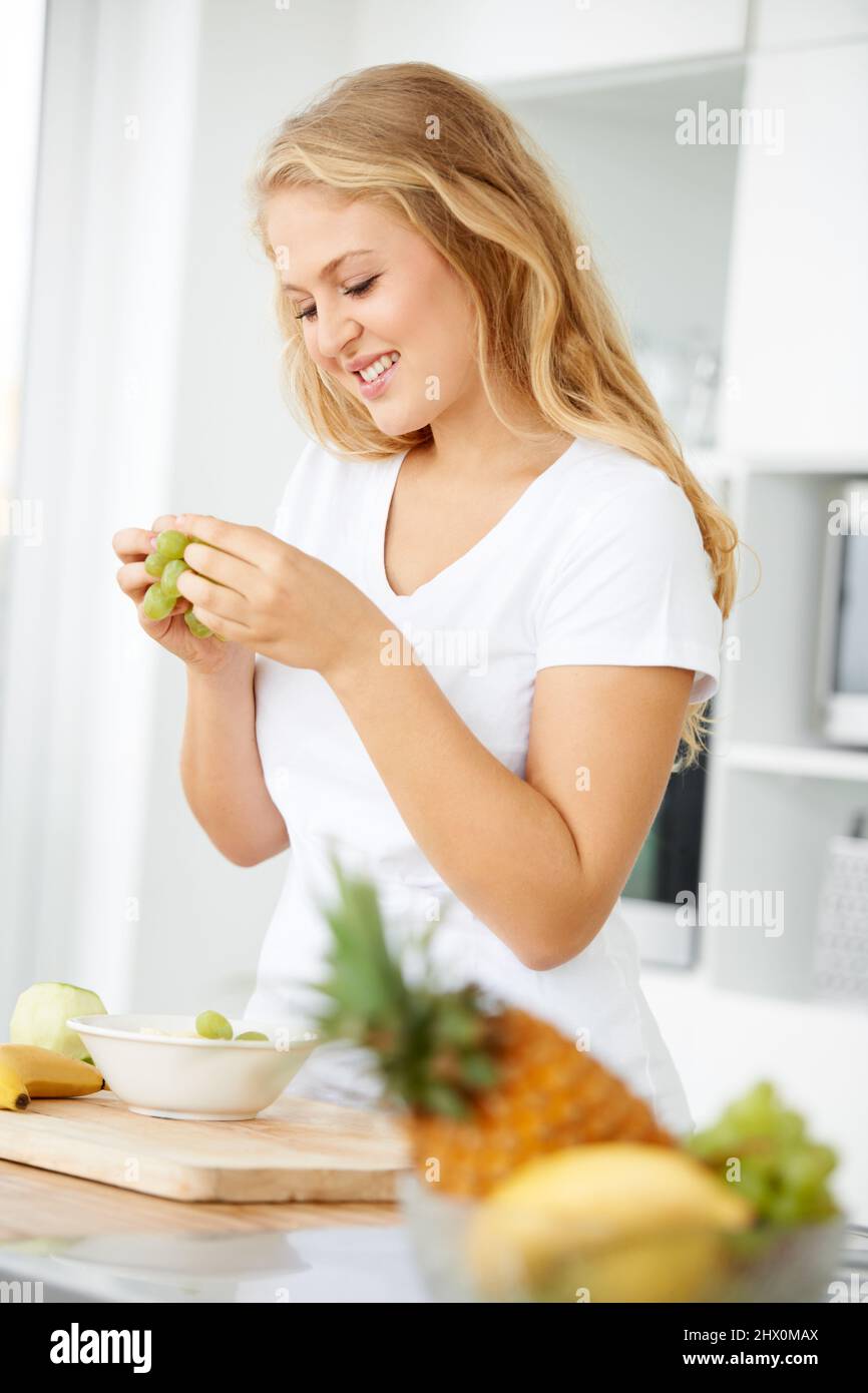 These grapes are so sweet. Curvaceous young woman eating grapes in her kitchen. Stock Photo