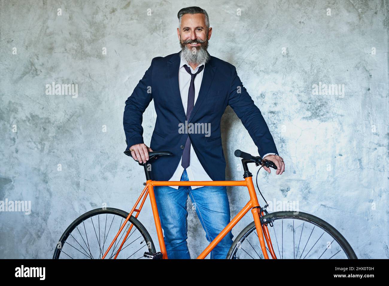 Off to go see the client. Studio shot of a confident middle aged businessman holding a red bicycle while standing against a grey background. Stock Photo