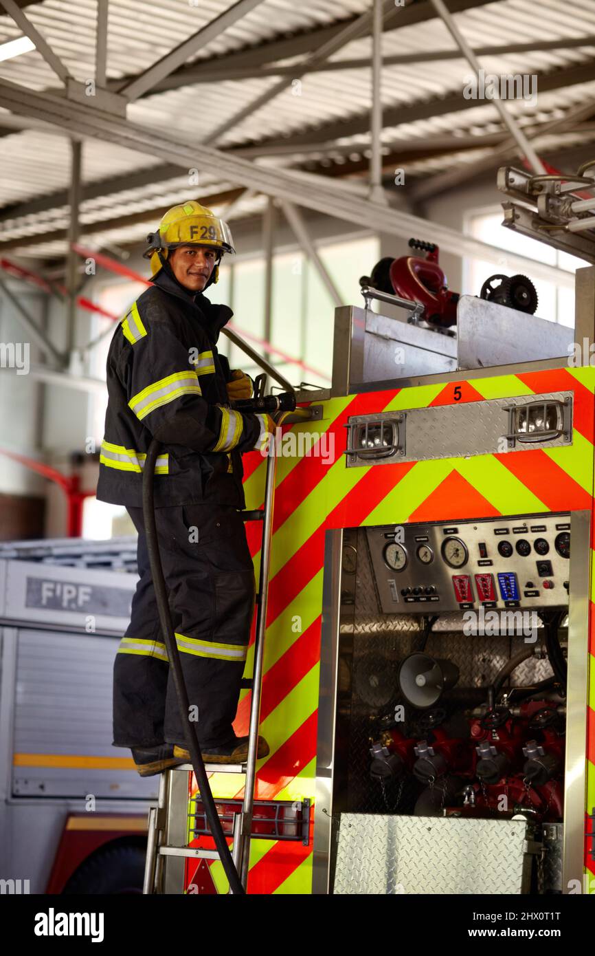 Keeping you safe from fire. A young male firefighter on the ladder at the back of a firetruck. Stock Photo
