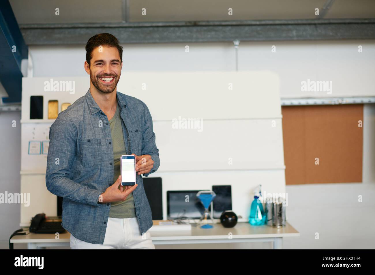 Proud to launch my new app for android phones. Portrait of a young man displaying the screen of a mobile phone in a modern office. Stock Photo