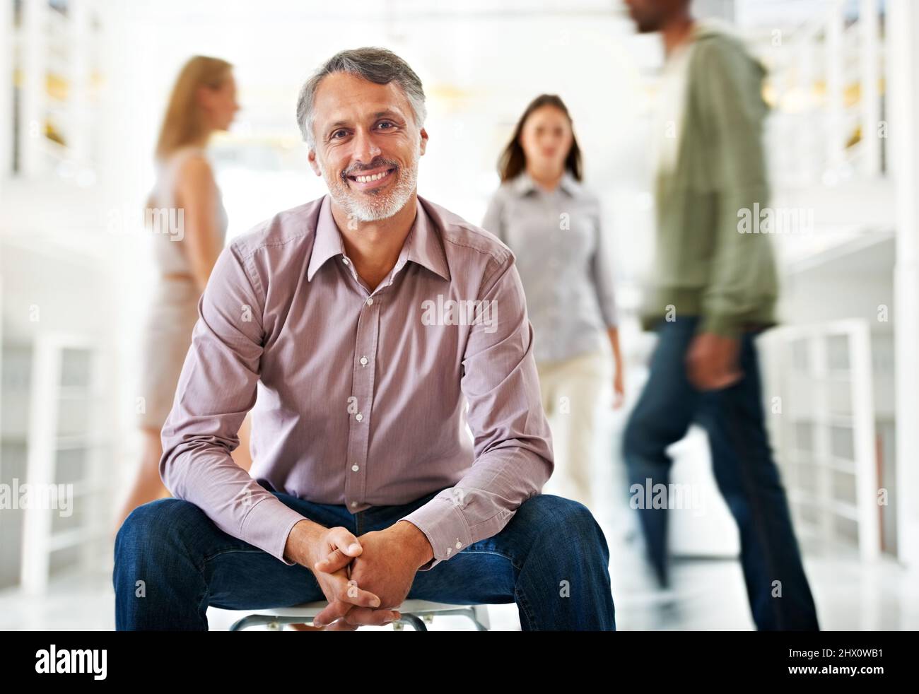 Level-headed leadership keeps him at the top. A handsome mature businessman sitting calmly as his colleagues stream by in haste - conceptual. Stock Photo