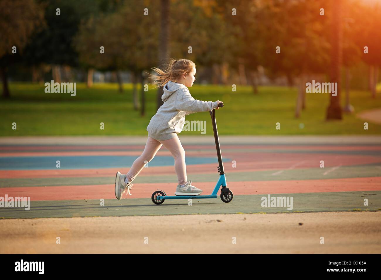 Portrait of active little toddler girl riding scooter on road in park outdoors on summer day. Seasonal child activity sport Stock Photo