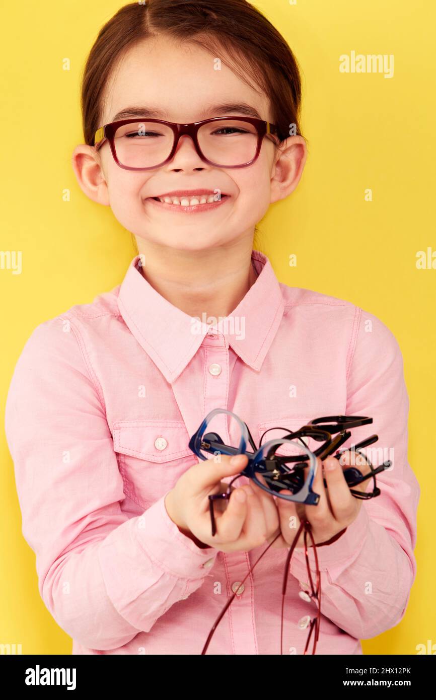 Look how many I have. A cute little girl standing against a yellow background with a hand full of glasses. Stock Photo