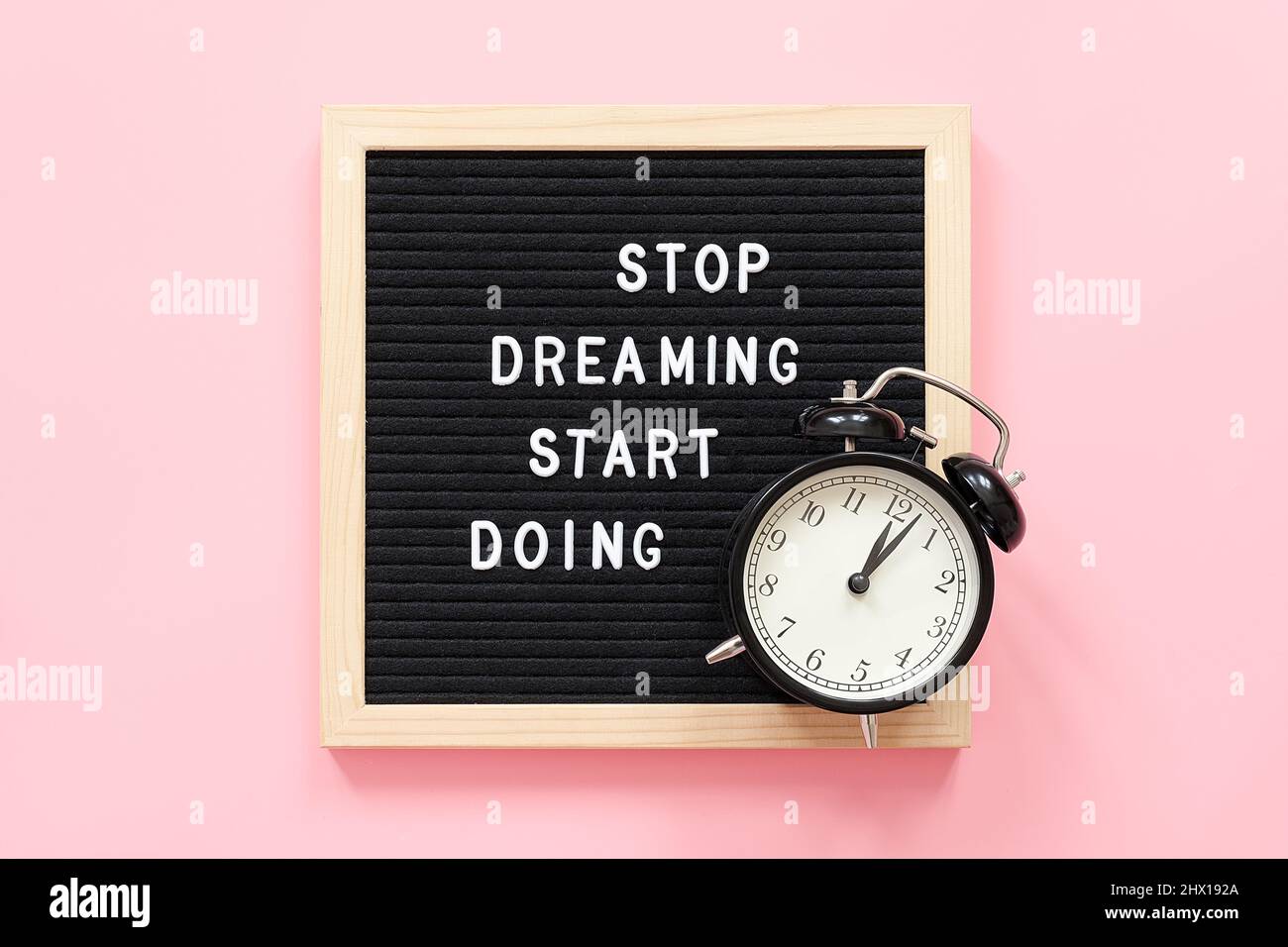Stop Dreaming Start Doing. Motivational quote on frame letter board and black alarm clock on pink background. Top view Flat lay Concept inspirational Stock Photo
