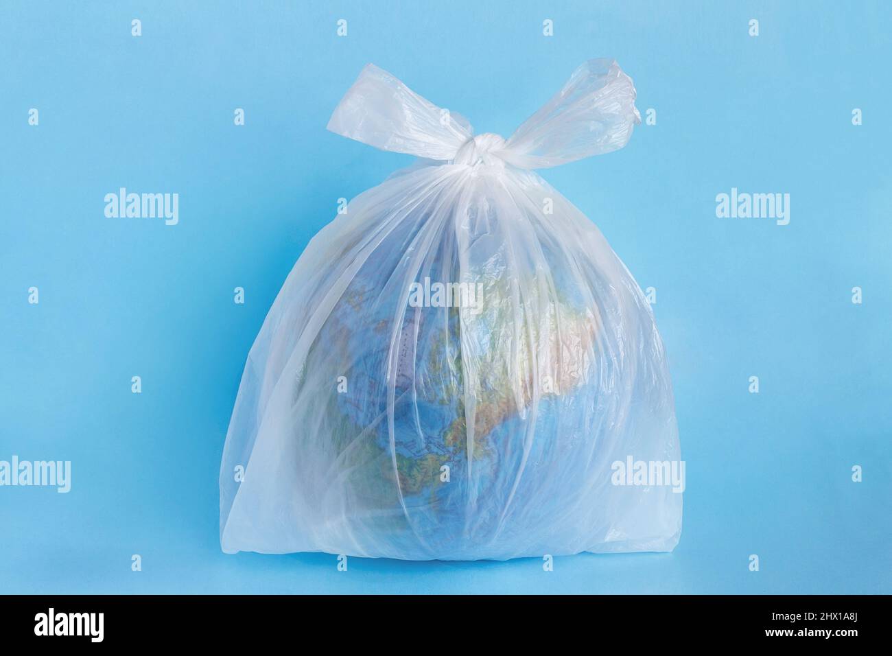 Model planet Earth in polyethylene plastic disposable package blue background. Ecology problems Concept pollution of environment with polyethylene pla Stock Photo