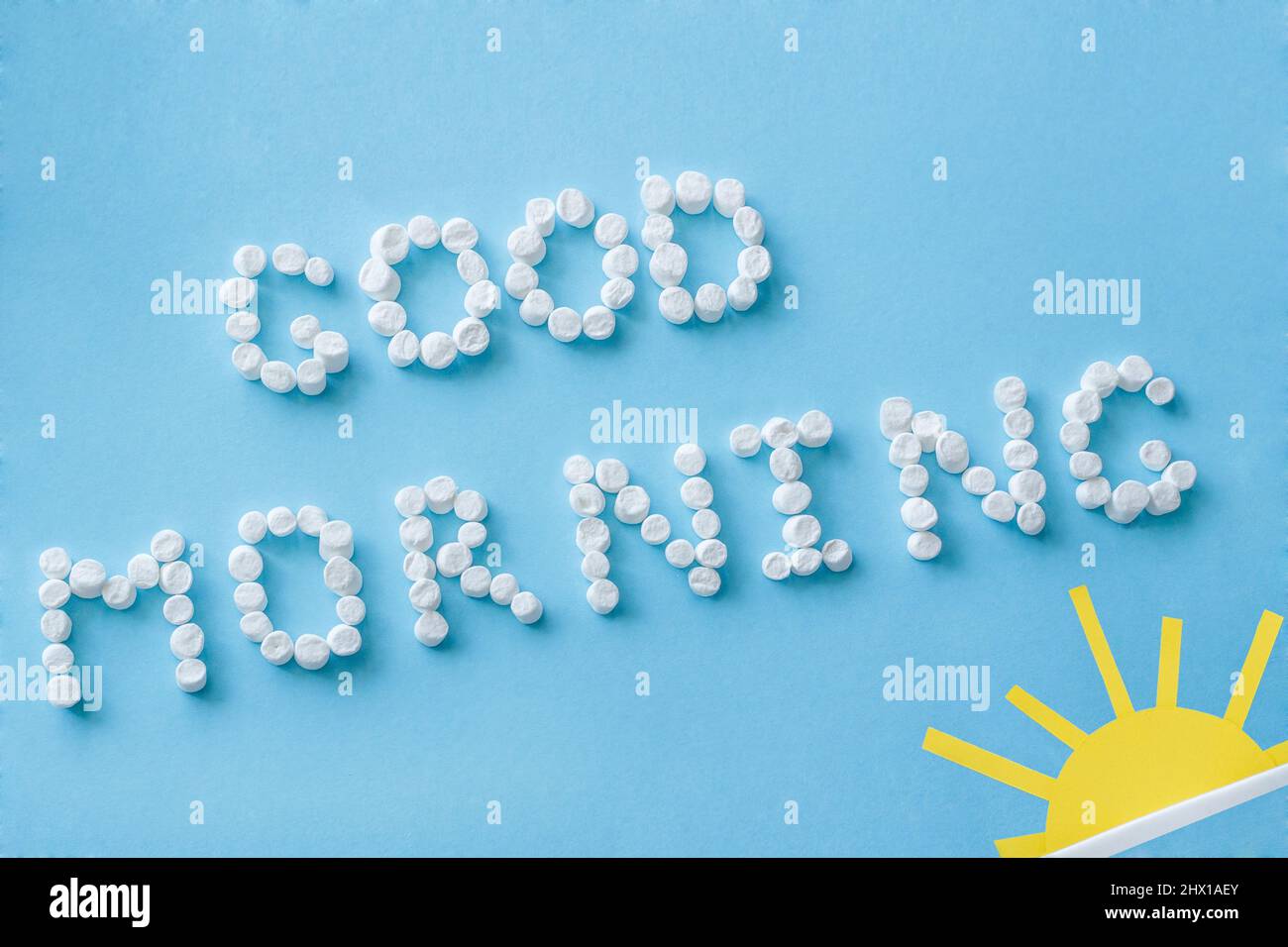 Text 'Good Morning' from marshmallows and figure of rising sun on blue background. Concept Stock Photo