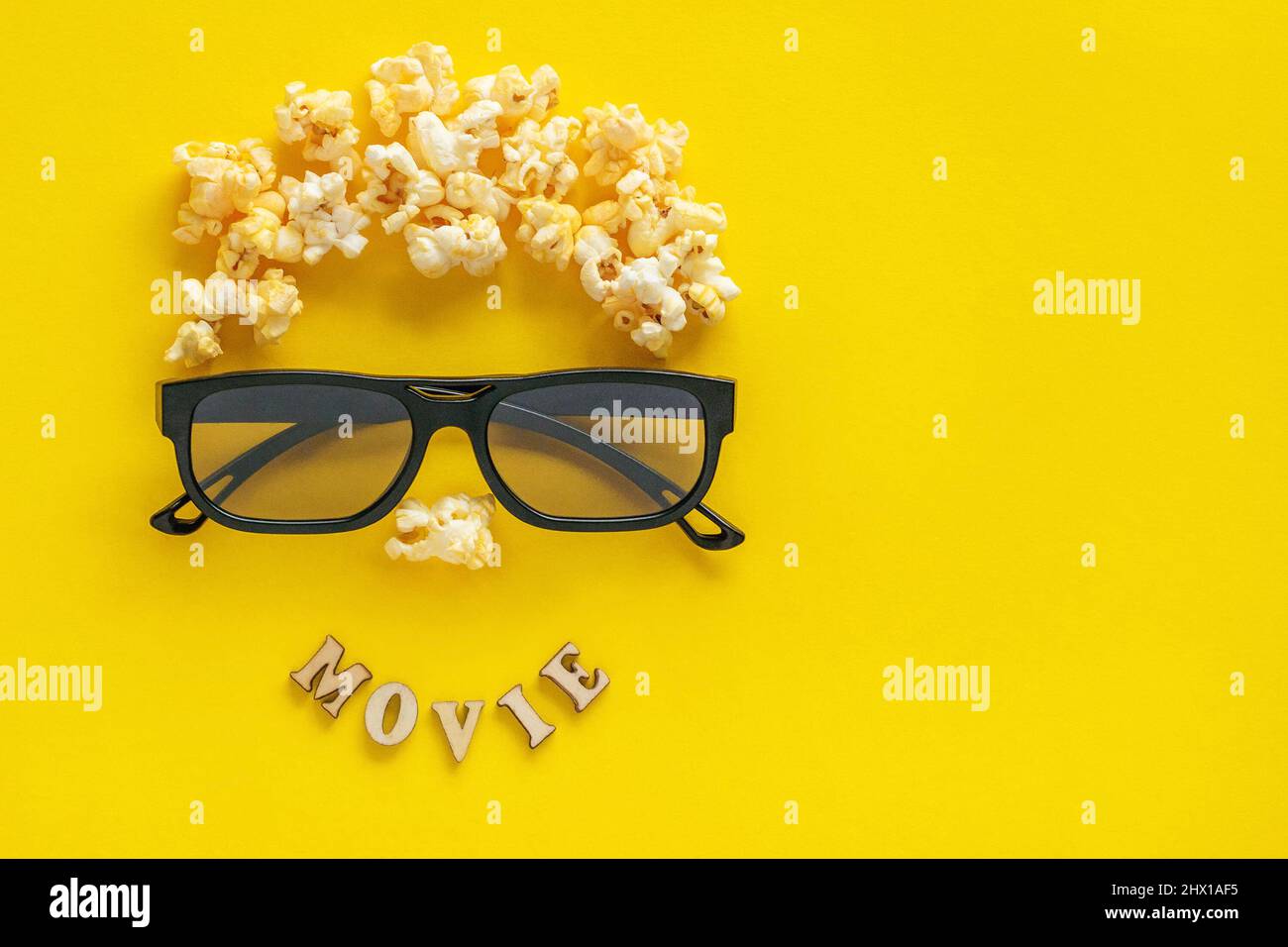 Abstract image of viewer, 3D glasses and popcorn, text MOVIE on yellow background. Still life, top view, flat lay. Concept cinema and entertainment Stock Photo