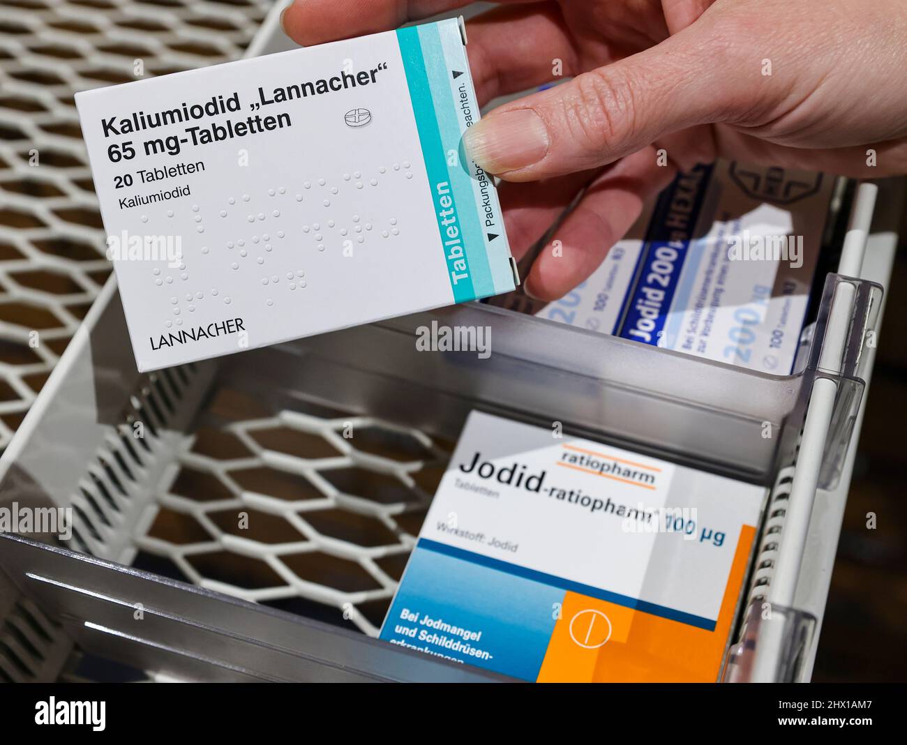 08 March 2022, Saxony, Leipzig: A pharmacist takes a pack of high-dose iodine tablets from a supply cabinet, next to which are weaker doses for thyroid disorders. The increased demand for iodine tablets due to the war in Ukraine could lead to problems for patients with thyroid diseases. Certain preparations are no longer available, the Saxon Pharmacists Association informed on request - and warned against a preventive intake of low-dose iodine tablets. The authorities responsible for disaster control have stockpiled around 190 million tablets in significantly stronger doses for this purpose. P Stock Photo