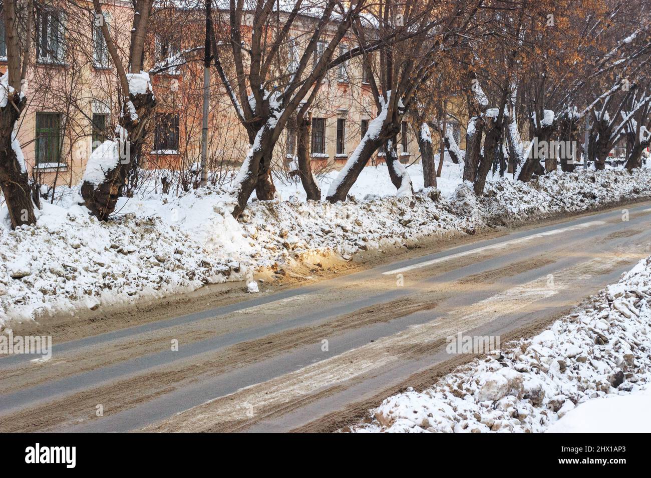 Dirty snow on the streets of the city in Siberia. Sand and reagents against icy condition. Stock Photo