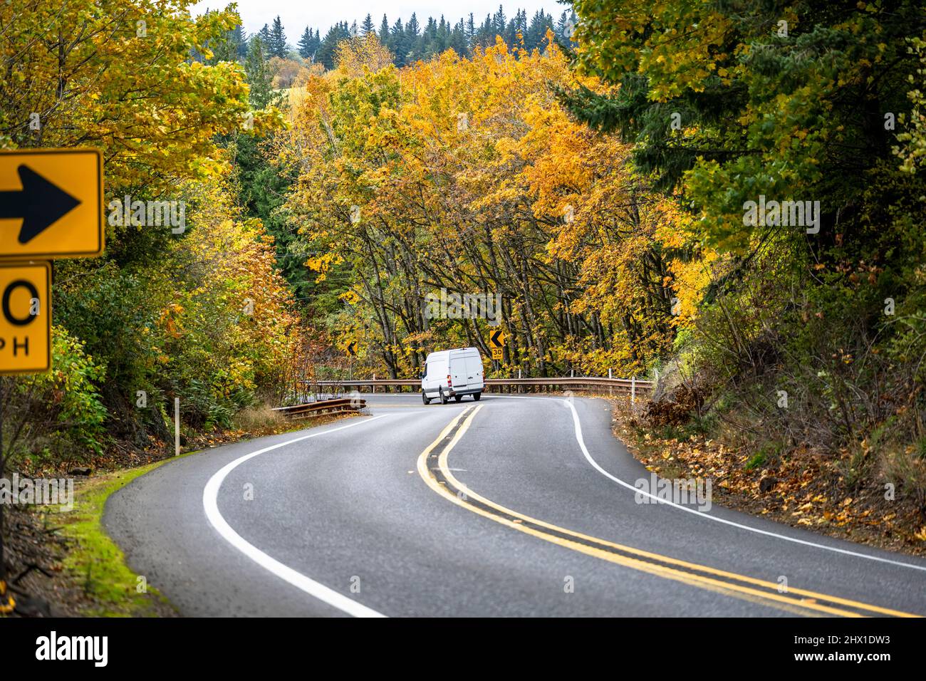 Compact industrial small size white mini van with high roof for comfort local delivery and small business needs running on the winding mountain autumn Stock Photo