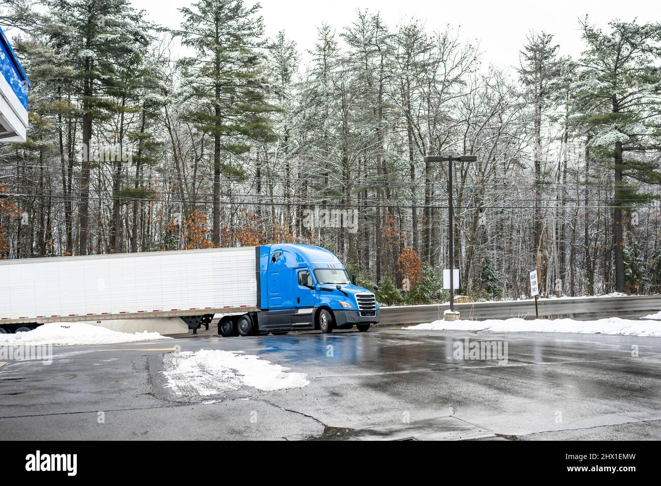 Industrial blue bonnet big rig long haul semi truck transporting cargo in refrigerator semi trailer turning on the truck stop entrance with snow and i Stock Photo