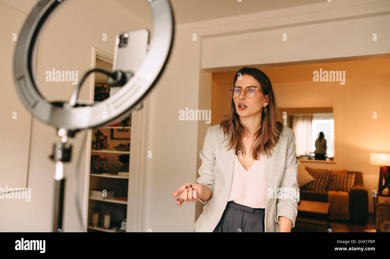 Influencer recording content for her social media channel. Female blogger speaking in front of a ring light and a camera phone. Freelancer creating a Stock Photo
