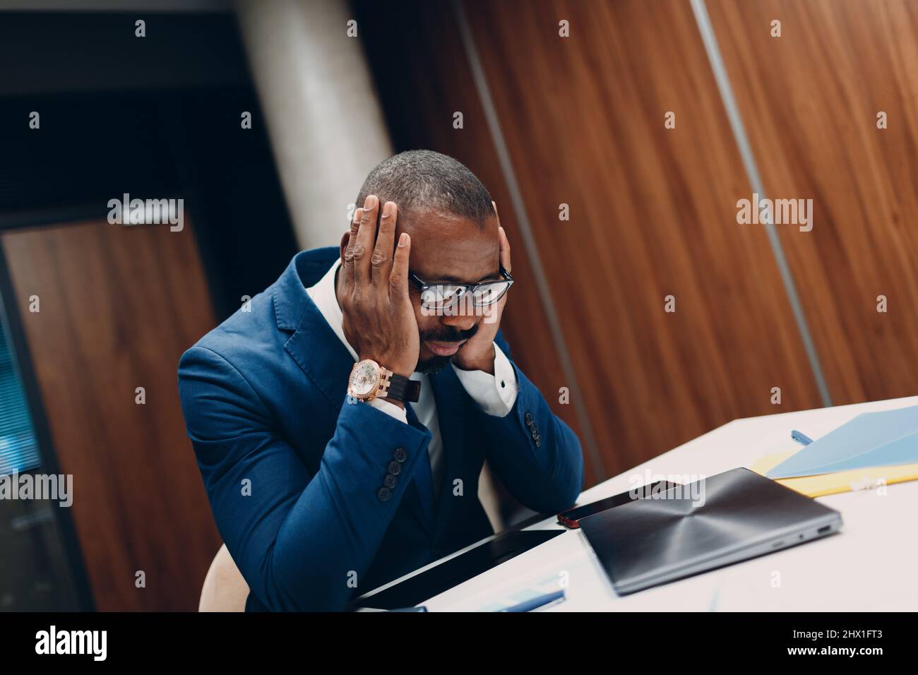 Concept economic sanctions, financial crisis and bankruptcy. Sad african american black Businessman sit and hold head with his hands at office table. Stock Photo
