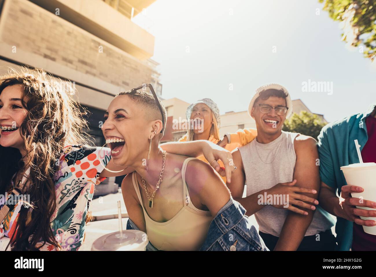 Enjoying friendship and youth. Group of generation z friends laughing cheerfully while walking together in the summer sun. Happy young friends having Stock Photo