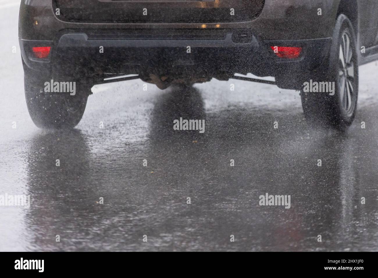rain water splash flow from wheels of black car moving fast in daylight