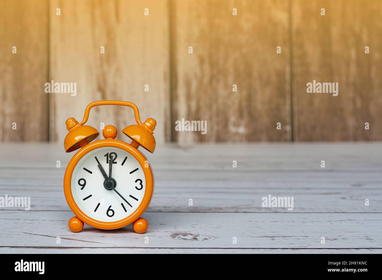 Orange alarm clock isolated on wooden desk. The clock set at 11 o'clock. Deadline concept. Stock Photo