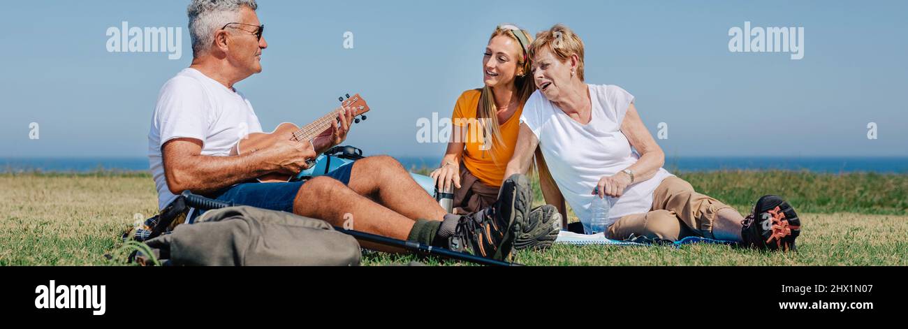 Adult family playing ukulele and singing sitting on a blanket during an excursion Stock Photo