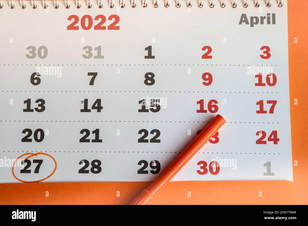 A close-up reminder of the memorable date recorded in the calendar on APRIL 27, a white paper calendar on an orange background with an orange marker. Stock Photo