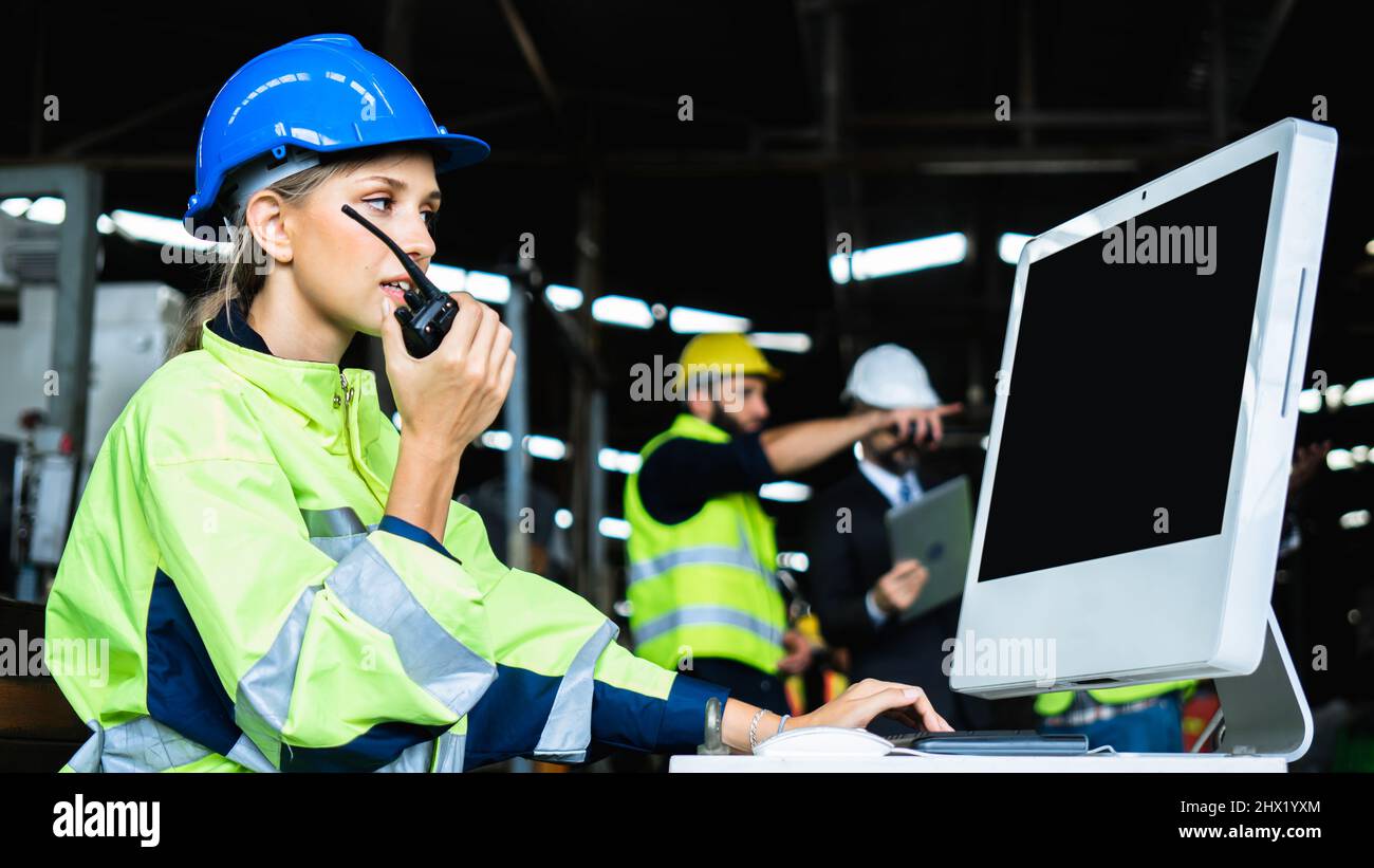 Mechanical engineer woman holding radio working industry wearing safety reflective vest and blue helmet, inspector standing control industrial machine Stock Photo