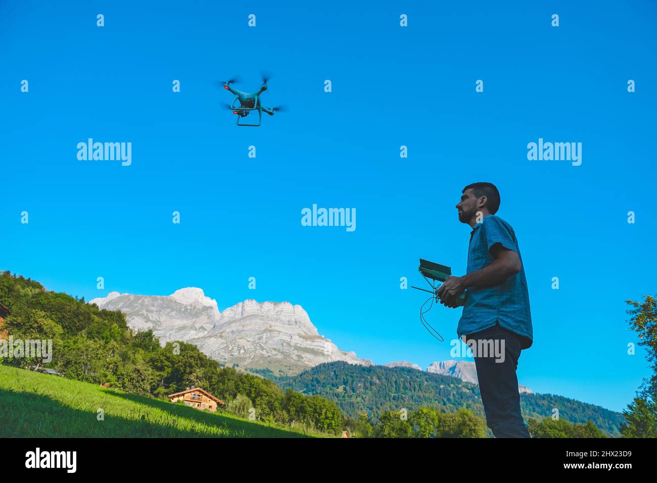Young man flying drone on amazing mountain landscape. Man operating a drone with remote control taking aerial photos and videos. Stock Photo