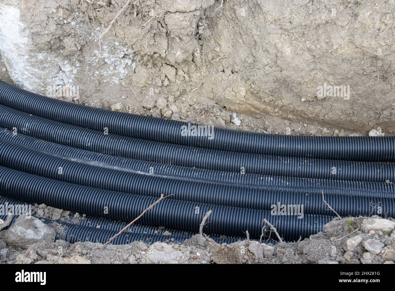 Black corrugated plastic drainage pipes laying in a ditch at a