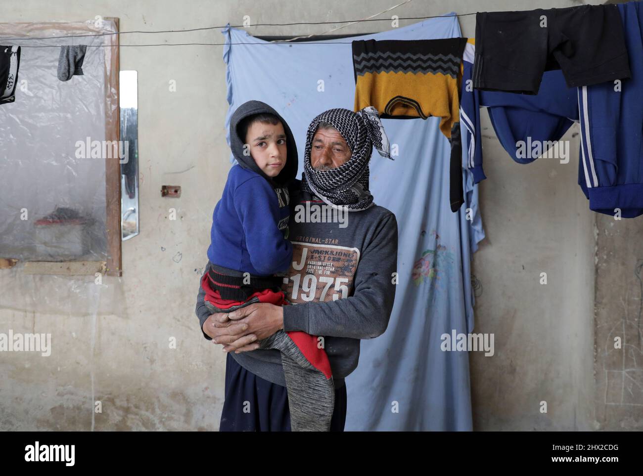 Mahmoud Madarati, 55, stands at home as he holds his son whose leg and hand were amputated after sustaining injuries by what Mahmoud says was shelling from government-held areas seven months ago, in the rebel-held town of Tadef, on a frontline between Russian-backed Syrian government forces and Turkey-backed Syrian rebel-held territory, northern Syria March 3, 2022. Picture taken March 3, 2022.  REUTERS/Khalil Ashawi Stock Photo
