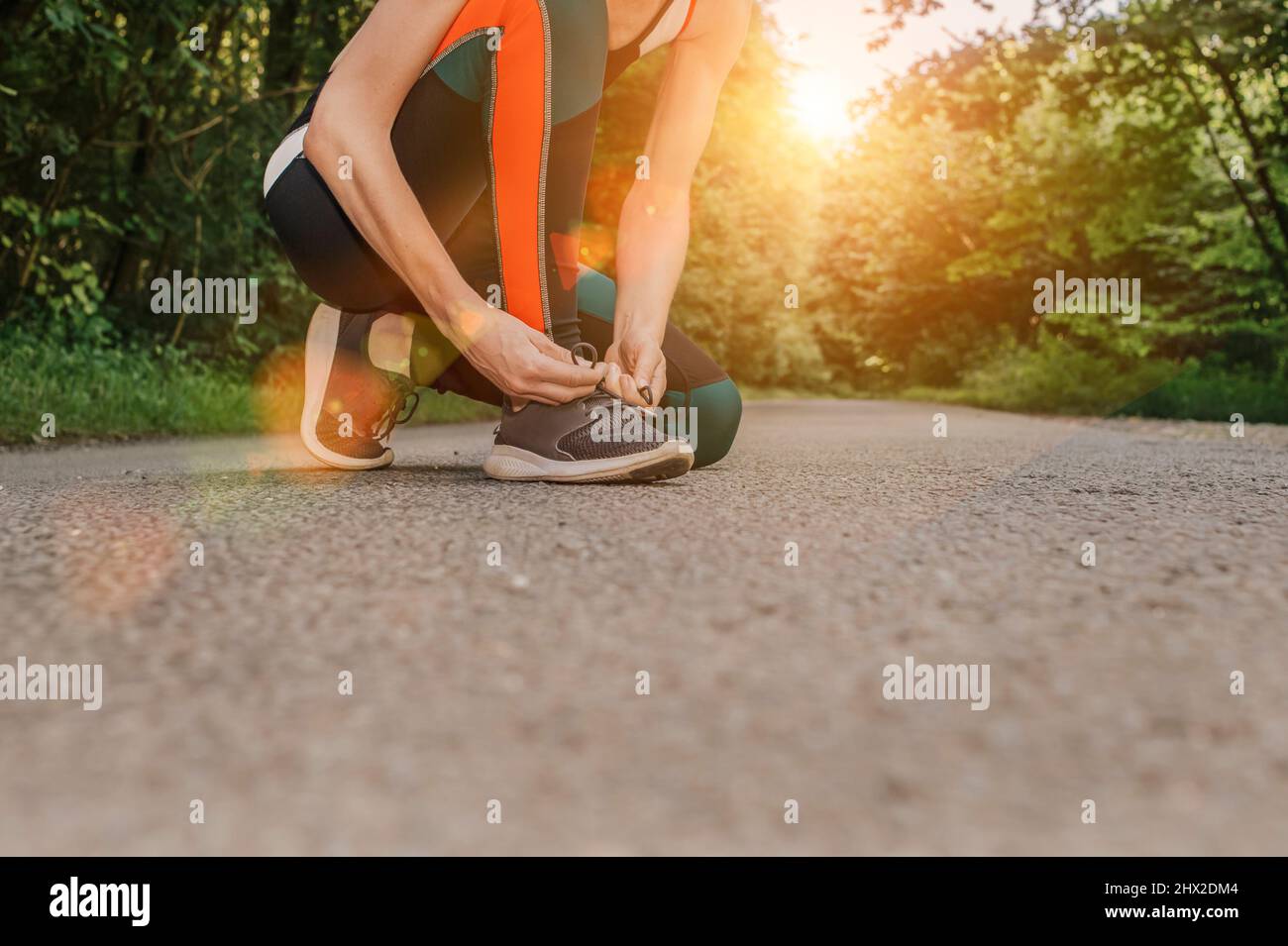 Woman runner tying shoelaces on her shoes before running on the road Stock Photo