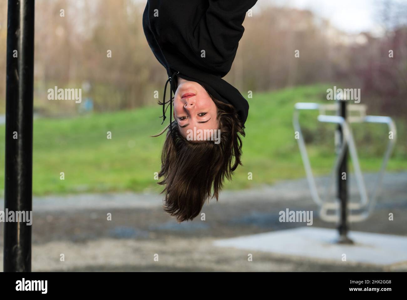 White teenage girl with brown hair hanging upside down like a bat on a climbing frame Stock